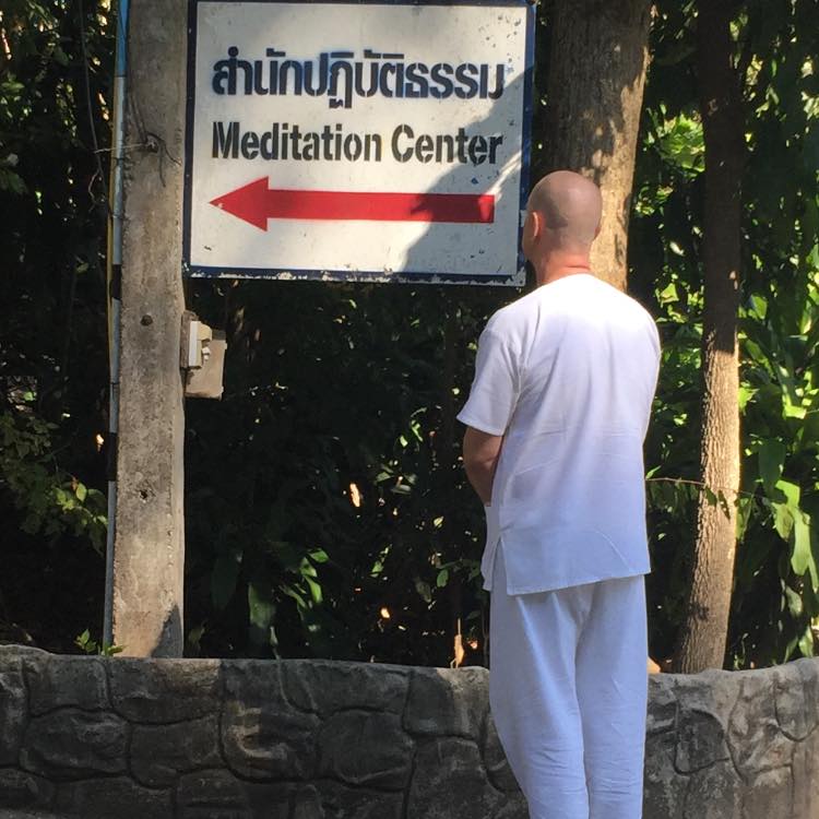 Teacher David Roylance in white clothing, facing away toward a meditation center sign